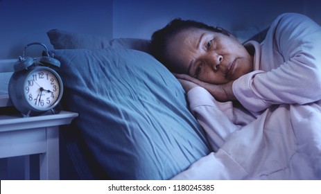 60s Or 70s Asian Senior Woman Having Sleep Disorder, Sitting In Bed Look Sad.Lonely Grandmother Have Difficulty Falling Asleep. Waking Up Often During The Night And Having Trouble Going Back To Sleep.