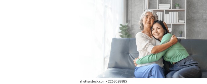 60s asian mother elderly sitting on sofa with young asia female daughter together in living room. hugs with love and encouragement - Shutterstock ID 2263028885