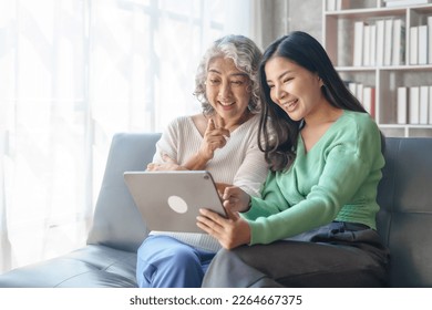 60s asian mother elderly sitting on sofa with young asia female daughter together in living room. watch movies series online or shopping, using tablet computer - Powered by Shutterstock