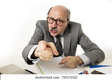 60s bald senior office boss man furious and angry gesturing upset and mad sitting on desk with paperwork in business and job problems and stress concept isolated on white background
