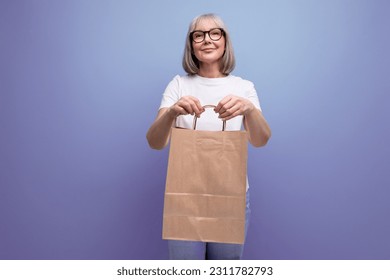 60s woman with gray hair holding kraft eco friendly bag on studio background - Shutterstock ID 2311782793
