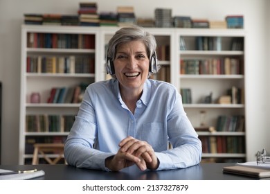 60s Woman In Headphones Sit At Table Staring At Camera Smile Enjoy Remote Video Conference Talk To Client Or Family Living Abroad. Virtual Meeting, Provide On-line Counselling, Communication Concept