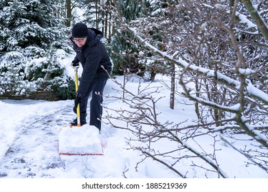 A 61-year-old Elderly Caucasian Man Clears Snow From A Courtyard With An Orange Shovel. Healthy Lifestyle Concept In Old Age