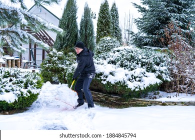 A 61-year-old Elderly Caucasian Man Enthusiastically Throws Snow In The Yard With An Orange Shovel. Healthy Lifestyle Concept In Old Age