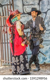 6-2-2019 Muskogee USA - Older Heavy Woman Dressed In Steampunk With Hat And Skull Skirt Flirts With Man Dressed Mostly In Leather With Beard And Hat And Black Fan In Front Of Fake Castle Wall.