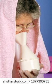 Femme de 65 ans avec serviette sur tête inhalant de la vapeur d'huile essentielle en tant que thérapie de substitution
