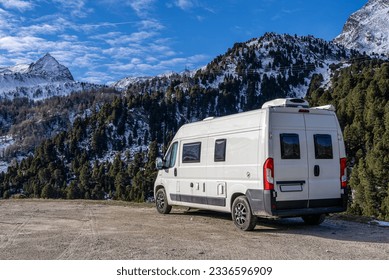 6m long white camper van in the mountains. The Camper is parked in an unpaved square and you can see the rear and the left side. The VanLife in the mountains in Switzerland.