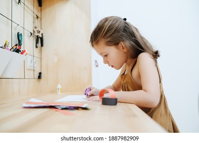 A 6-year-old Girl Sits At A Table, She Glues A Garland Of Paper. Real Life Moment