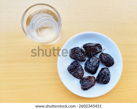 7 dates in a small white plate and a glass of water. 