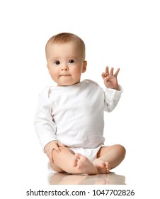 7 Month Infant Child Baby  Girl Toddler Sitting In White Shirt With Hand Up Show Ok Sign Isolated On A White Background