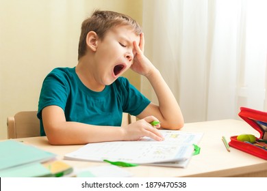 7 yeas old boy sitting at desk and doing homework. Child write notes in notebook, difficult homework, child concentrating on examples - Powered by Shutterstock