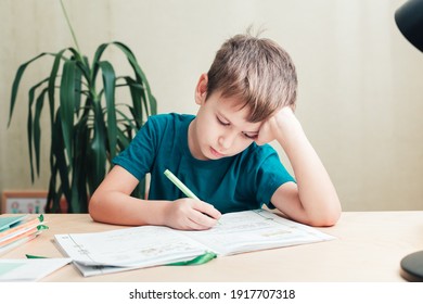 7 yeas old boy sitting at desk and doing homework. Child write notes in notebook, difficult homework, child concentrating on examples - Powered by Shutterstock