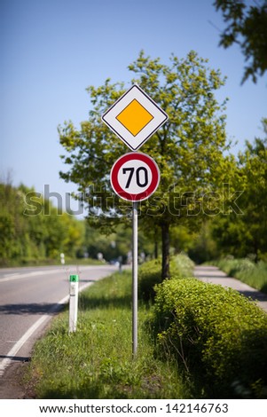 70 kilometres per hour speed sign and priority or right of way yellow diamond on a pole at the side of a rural road or route