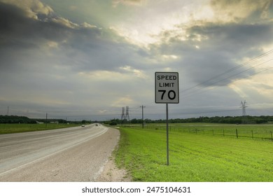 A "70" speed limit sign commands attention along a Texas highway, on a road trip, stretching endlessly beneath a dramatic sky filled with billowing clouds. - Powered by Shutterstock