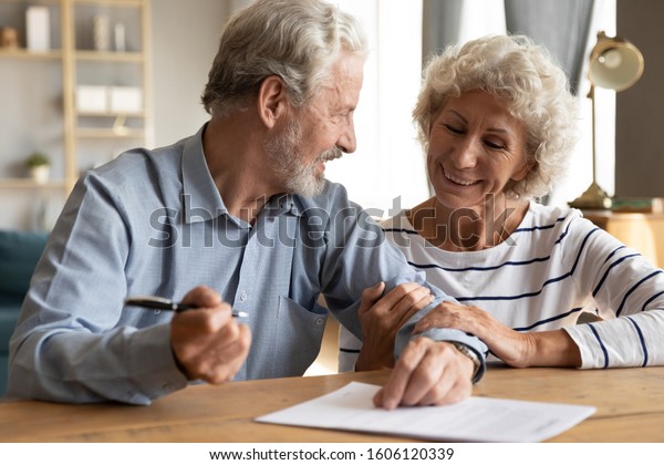 70s couple sit at table indoor discuss agreement\
term and condition feels satisfied make financial deal ready to\
sign contract, bequeath savings and property to their children or\
grandchildren concept