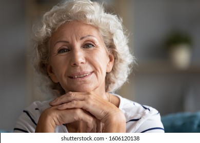 70s Grandmother Seated Indoors Posing Folded Arms Under Chin Looking At Camera, Representative Of Baby Boomer Generation, Older People Retired Well-being Life, Kindly Loving Granny Close Up Portrait