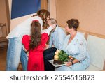 76-year-old man and 71-year-old woman celebrate their golden wedding anniversary, sitting on a sofa in the registry office with gifts. Their granddaughters, one kissing grandfather, congratulate them