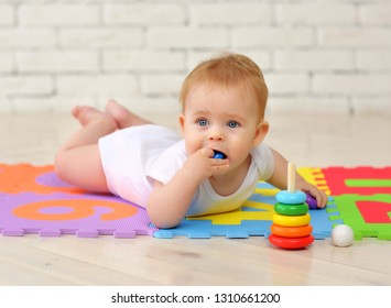 A 7-month-old baby plays on the floor with toys and stuffs small parts into his mouth. Security concept