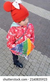 A 7-year-old girl in a red cap and jacket launches a kite in sunny weather on a large area. A child is playing alone on the street