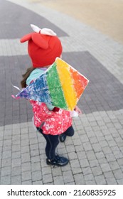 A 7-year-old girl in a red cap and jacket launches a kite in sunny weather on a large area. A child is playing alone on the street