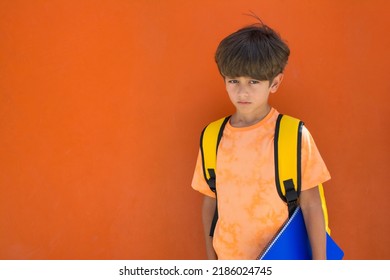 7-year-old School Child With A Sad Gesture With A Yellow Backpack, On An Orange Background. Image With Copy Space. Back To School.