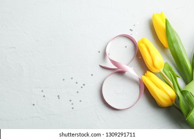 8 March, International Women's Day. Figure eight of pink ribbon with beautiful yellow tulips on gray background. Space for text