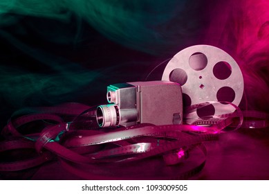 8 Mm Movie Camera With A Reel Of Film In Green And Purple Smoke. Dark Background