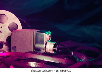 8 Mm Movie Camera With A Reel Of Film In Green And Purple Smoke. Dark Background