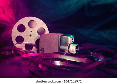 8 Mm Movie Camera With A Reel Of Film In Green And Purple Smoke. Dark Background