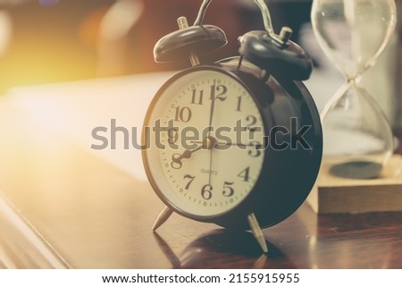 8 o'clock time retro clock with sand hourglass on wood table with sun light background