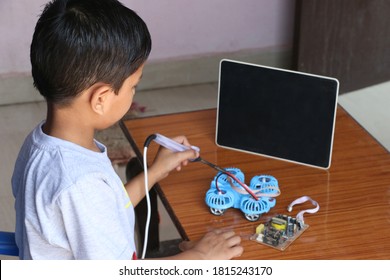 An 8 Year Old Child Is Learning To Make Drone In Online Coding Class With Black Screen Tab. Electric Soldering Iron In Kids' Hand. Closeup Image.  Concept Kids Coding Classes. Selective Focus Kids.