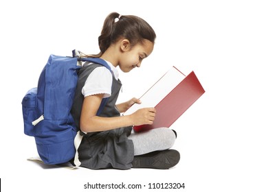 8 Year Old School Girl Sitting Reading Book With Backpack Smiling On White Background