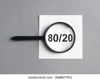 80 20 pareto principle concept, text through magnifying glass on gray background.
