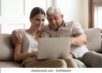 80s grandfather and adult 30s granddaughter sitting on couch look at pc screen interested with app or read news together surfing virtual space, younger generation teach older using modern tech concept - Powered by Shutterstock