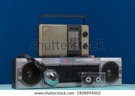 80s Retro outdated portable stereo cassette recorder and radio receiver, headphones, audio cassette on classic blue background. Attributes 80s, retro media, entertainment