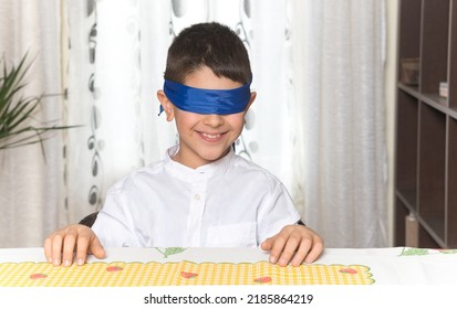 An 8-year-old Caucasian boy sitting at the table at home is blindfolded and smiling. - Powered by Shutterstock