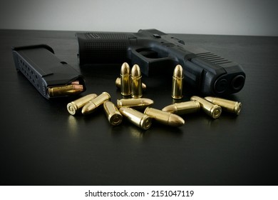 9 Mm Handgun With Fully Loaded Magazine And Bunch Of Golden Brass Ammo Spilled On Black Wooden Desk