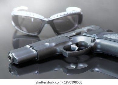 9 mm pistol with luger ammunitions and Shooting Safety Glasses on a black mirror base.