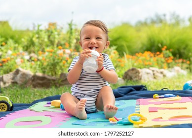 9 months old baby boy sitting in backyard, smiling and holding milk bottle. - Powered by Shutterstock