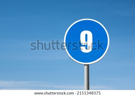 '9 (nine)' sign in blue round frame. Clear sky is on background