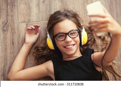 9 years old child is lying down on the floor, listening to music and taking selfie, top view point