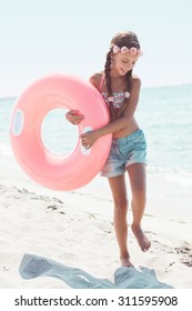 9 years old girl dressed in fashion floral swimsuit and denim shorts posing with inflatable ring at the beach in sunlight