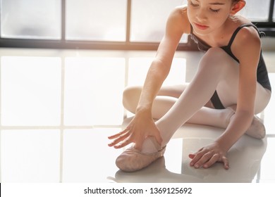 9 years old girl was sitting on the floor and tying ballet shoes for ballet class practice with the light from window background.
