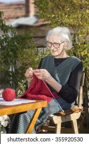 90 Years Old Woman Knitting A Red Sweater Outdoors