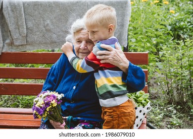 90s Years Old Senior Woman Great-grandmother Hugging Great-grandson. Kid Boy Supporting And Giving Flowers To Great-grandmother. Family Group, Support, Help, Connecting The Generations.