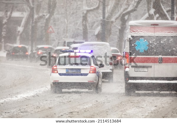 911 ambulance van and police\
car rushing through traffic during heavy winter snowfall\
conditions.