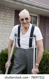 A 93 year old elderly man with crutches, standing alone outside his apartment with a big smile on his face