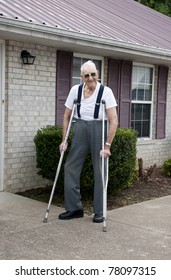 A 93 year old elderly man with crutches, standing alone outside his apartment with a big smile on his face