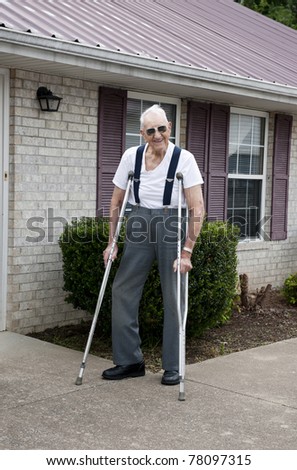 A 93 year old elderly man with crutches, standing alone outside his apartment with a big smile on his face