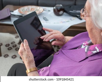 95 Year Old Woman Is Sitting In The Living Room And Is Typing On A Mobile Divice Or Ipad